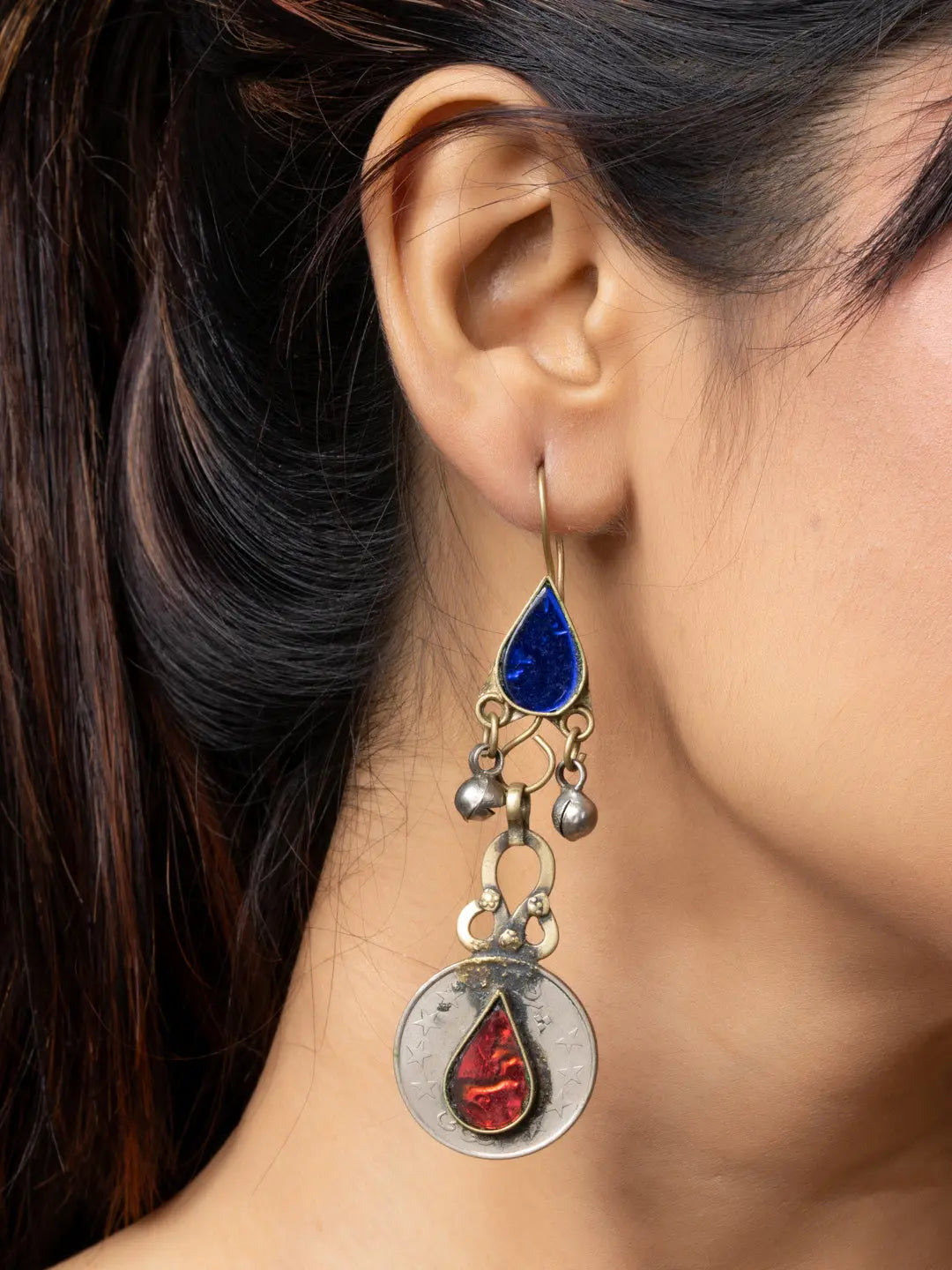 Close-up of a woman's ear wearing decorative afghani earrings with blue and red stones