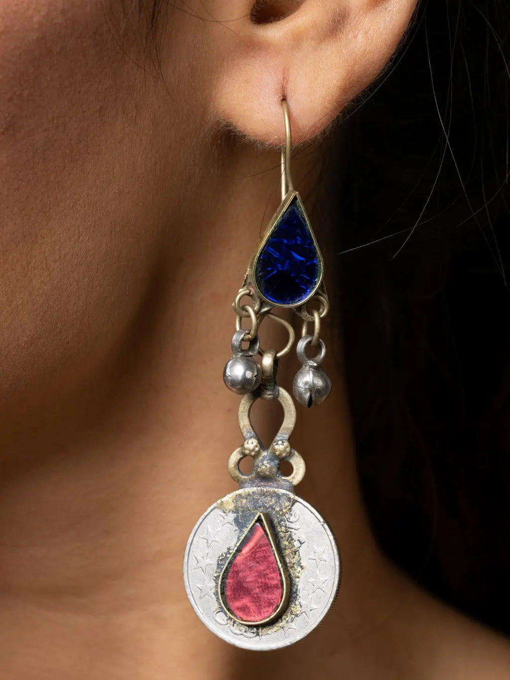 Close-up of a woman wearing handmade Afghani earrings with blue and red teardrop stones and silver detailing