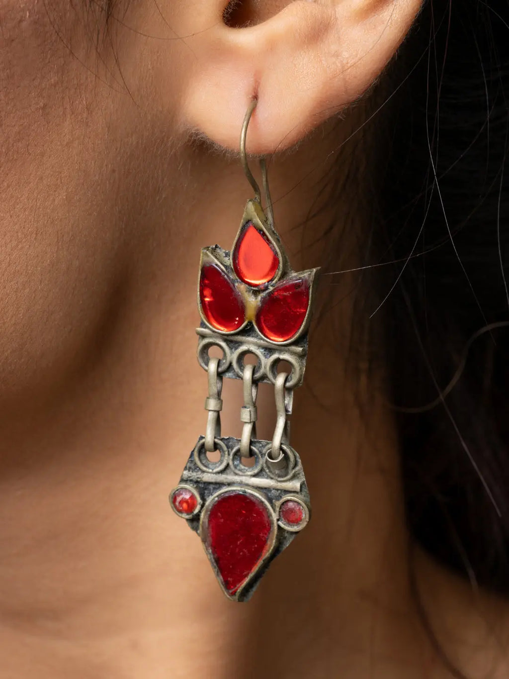 Close-up of afghani earrings with red stones and intricate silver design worn on ear