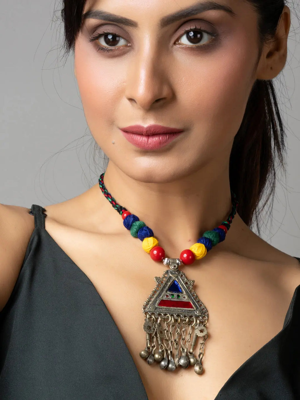 Colorful afghani necklace with a triangular pendant and dangling bells worn by woman