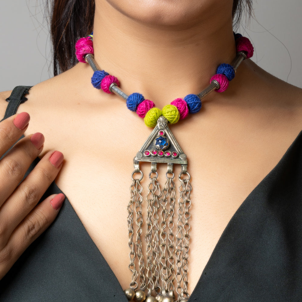 Colorful Afghani necklace with triangle pendant and hanging silver chains worn on woman in black dress