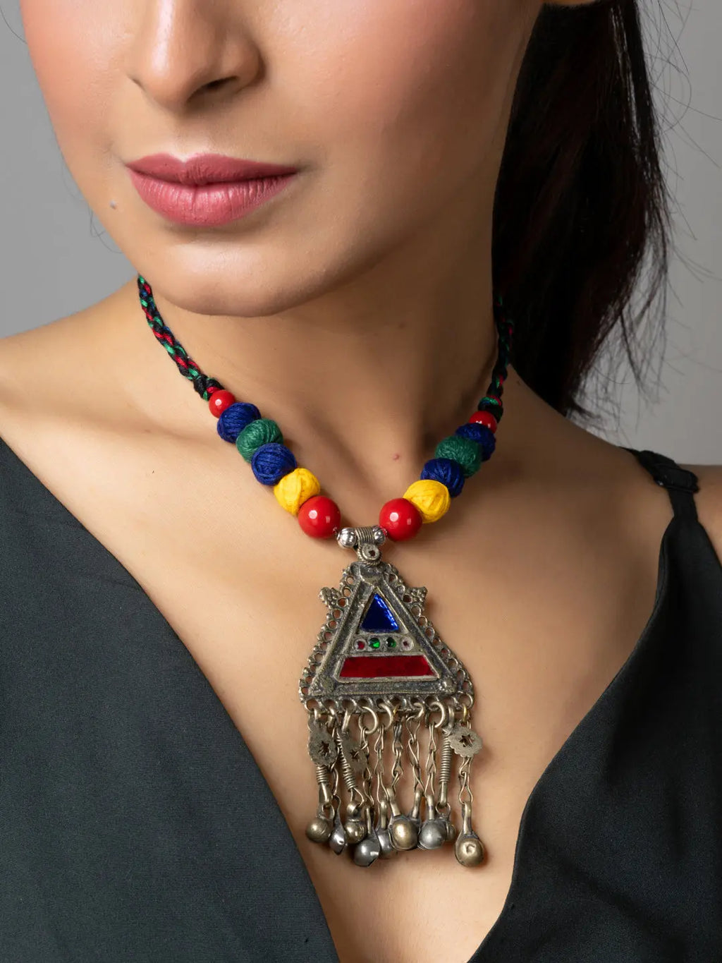 Colorful beaded afghani necklace with triangular silver pendant and dangling bells worn on model
