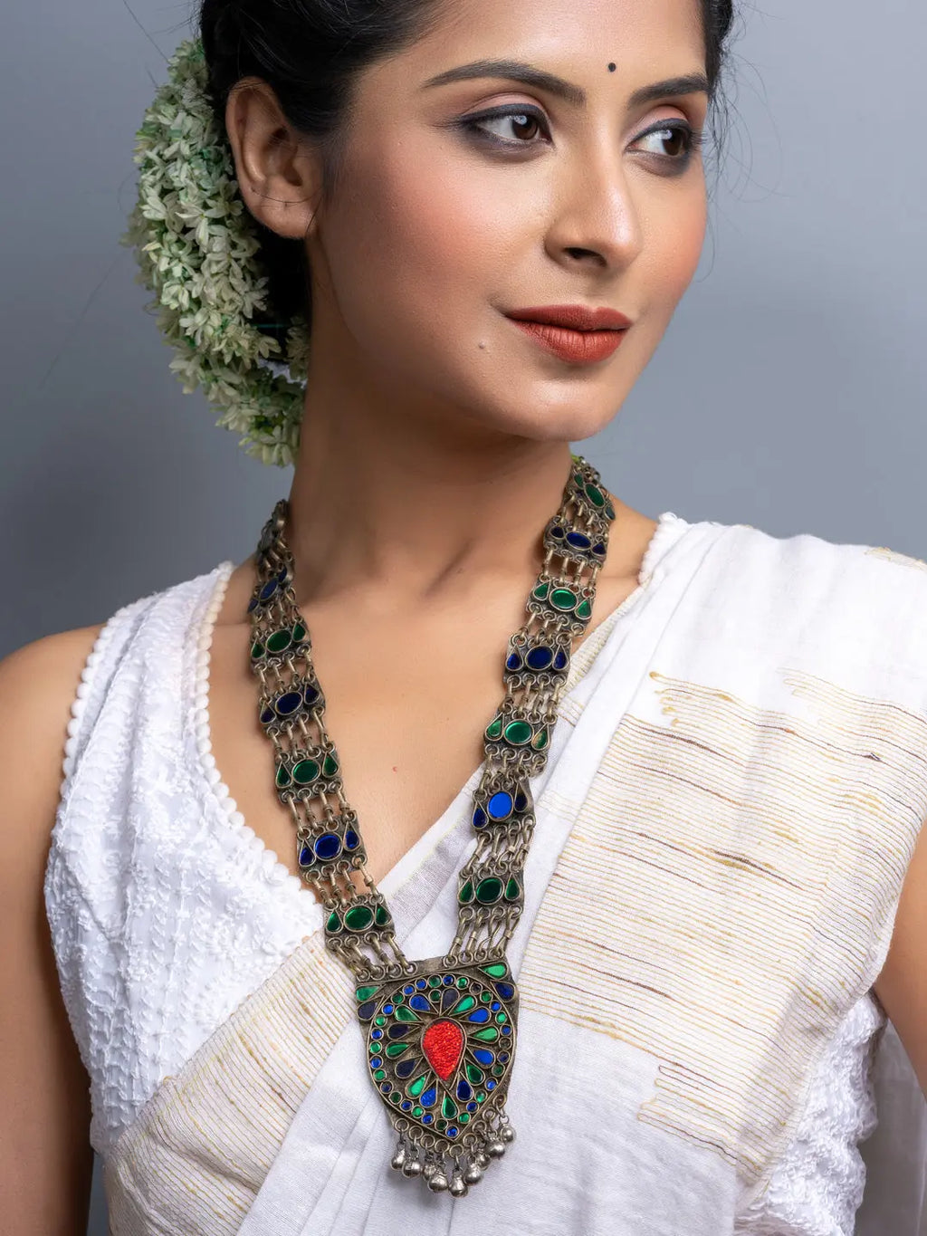 Afghani necklace with intricate blue and green stones worn by woman in white traditional attire