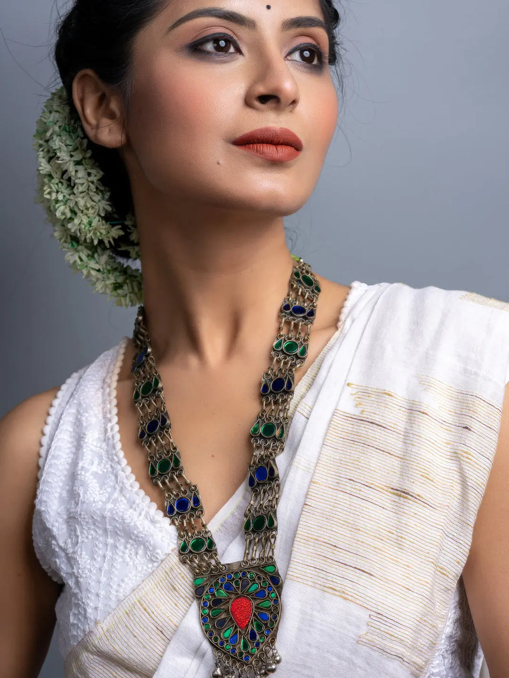 Woman wearing traditional afghani necklace with intricate green and blue stones and silver detailing
