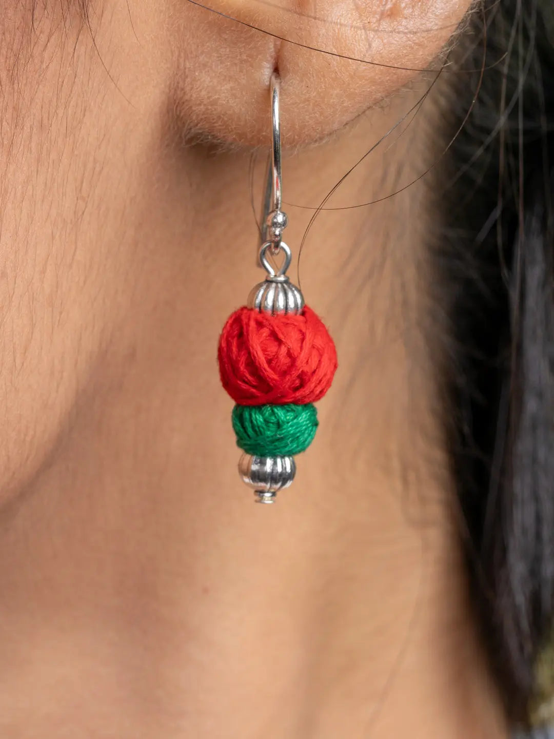 Close-up of a handmade Afghani necklace set earring with red and green thread beads hanging from a silver hook