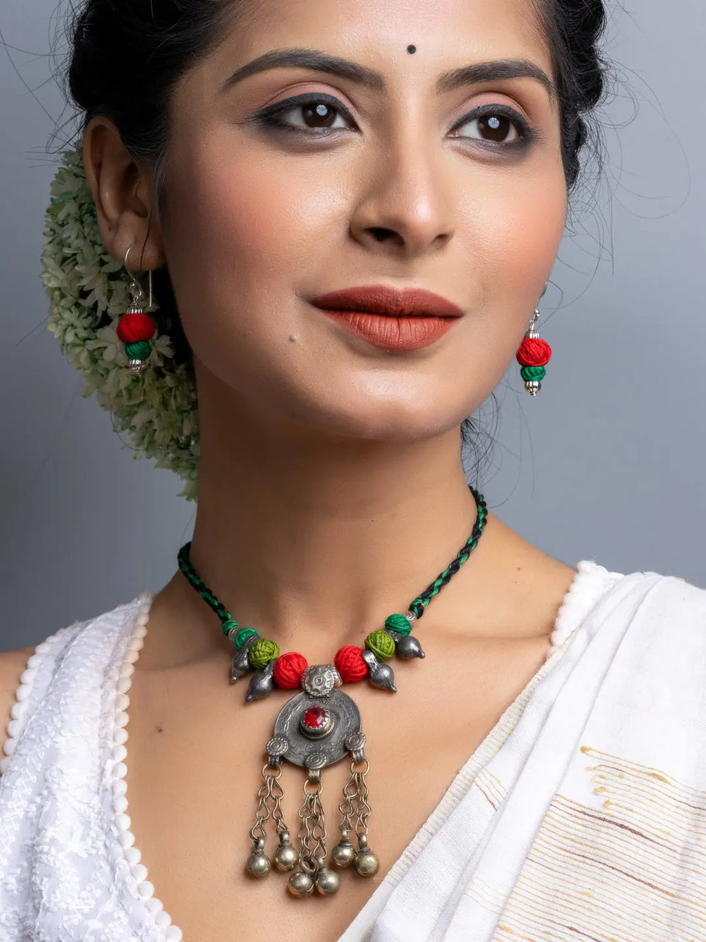 Traditional afghani necklace set with green and red beads and silver pendant worn by woman in white dress