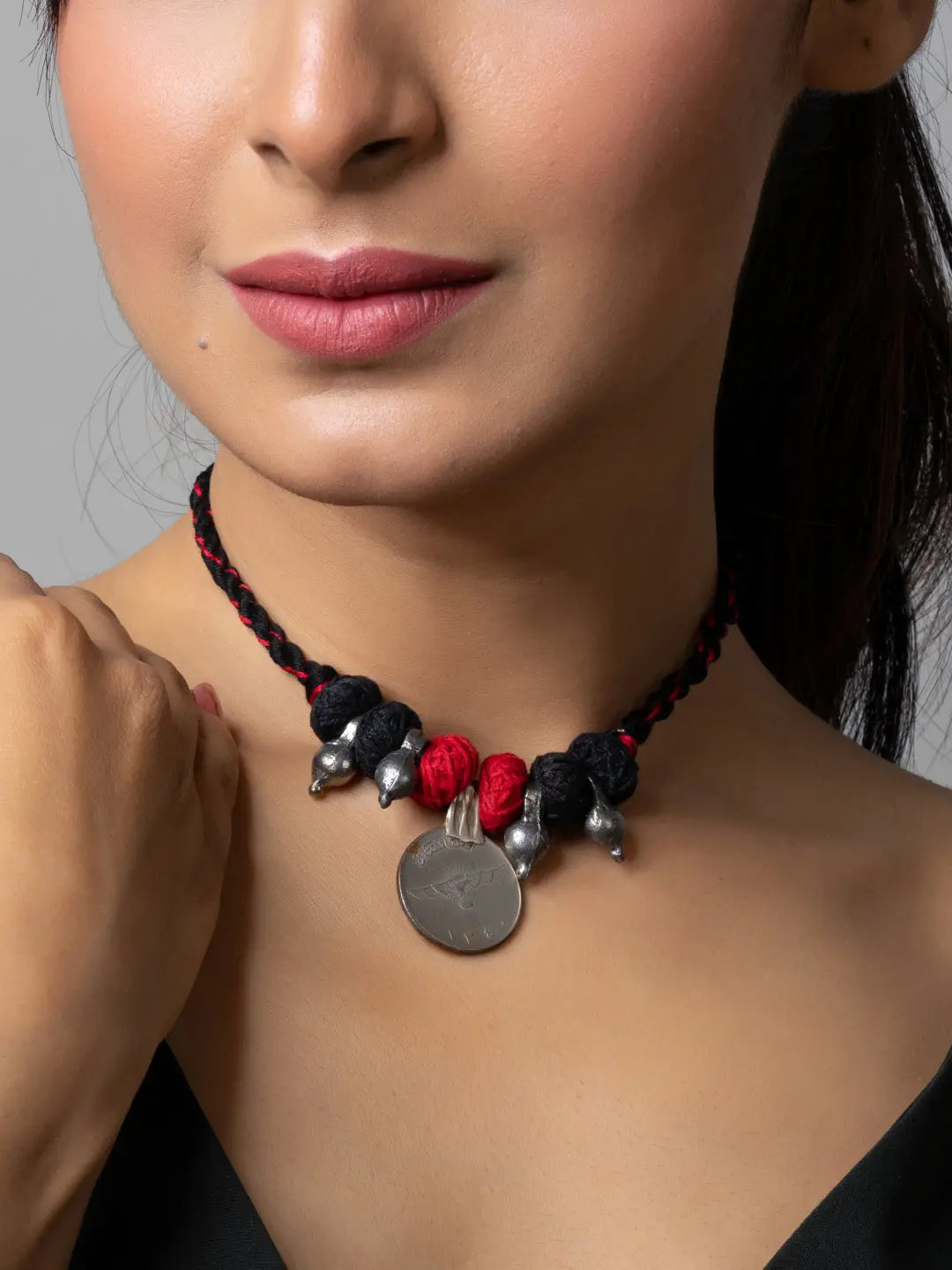Close-up of woman wearing handmade afghani pendant necklace with black and red braided cord and silver charms