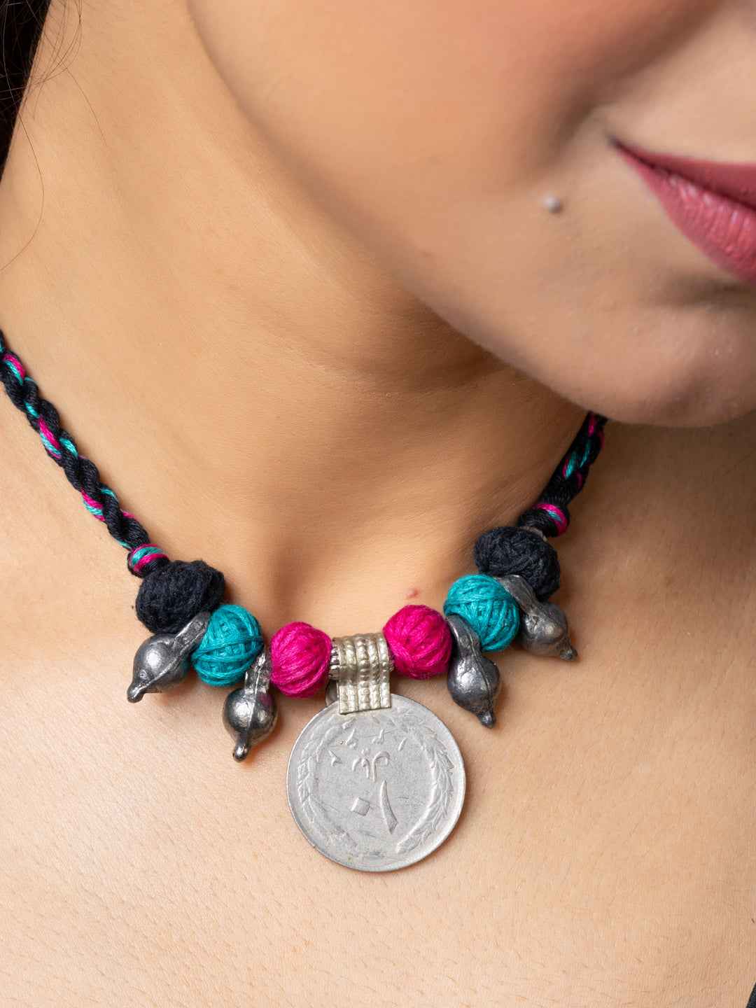 Close-up of colorful afghani pendant necklace with silver coin and braided black cord