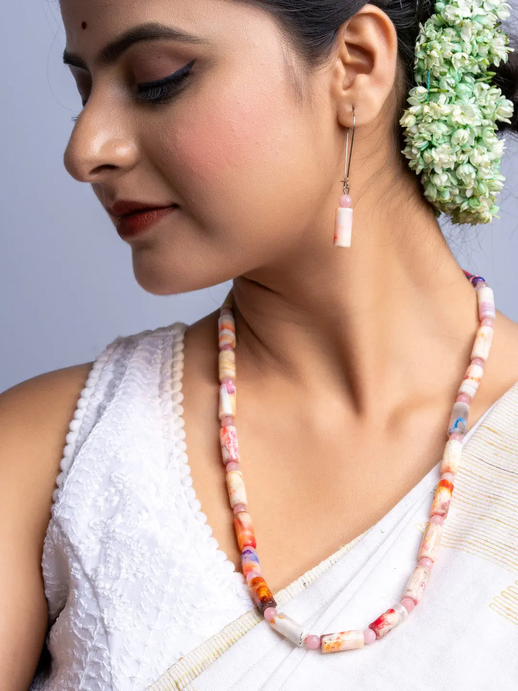 Handmade agate necklace with pink and orange beads worn by woman in white outfit with matching earrings