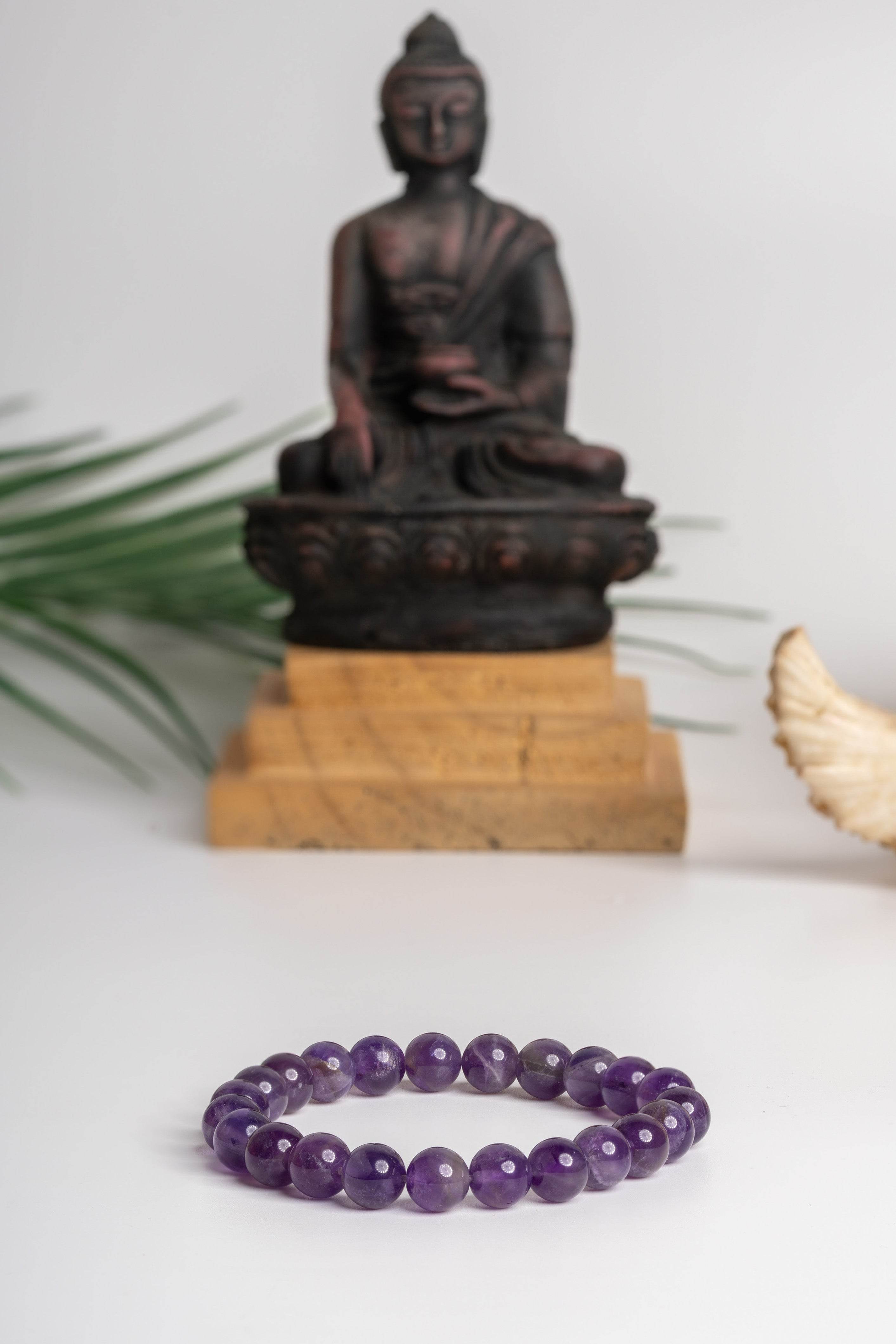 Amethyst stone bracelet featuring polished beads, with a serene Buddha statue in the background