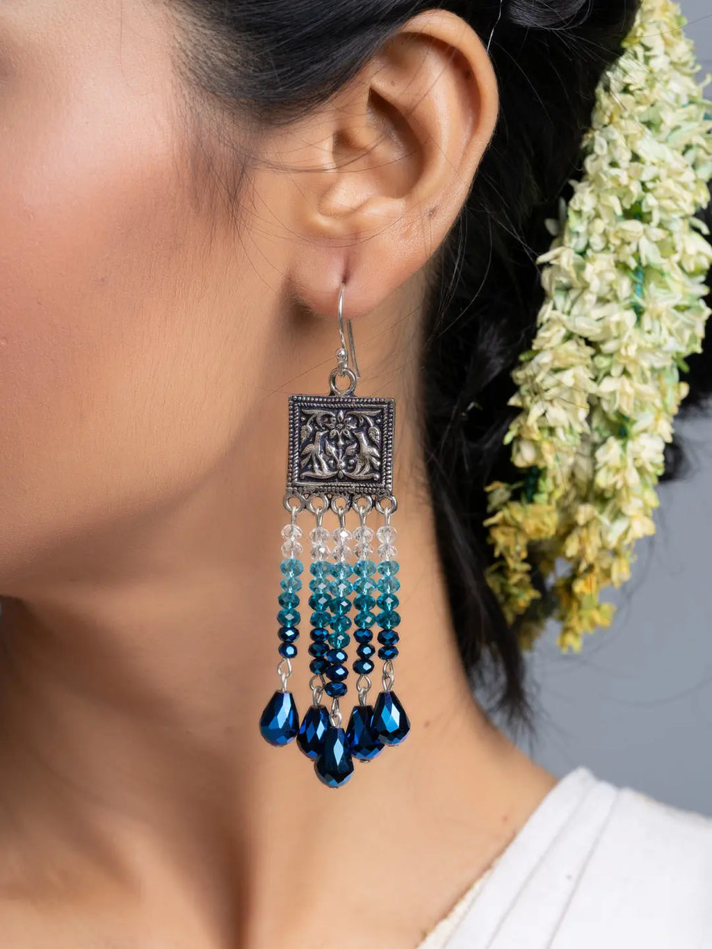 Handmade blue crystal earrings with intricate silver design worn by a woman with floral hair accessory