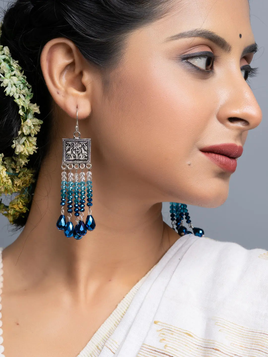 Woman wearing handmade blue crystal earrings with silver square design and dangling beads