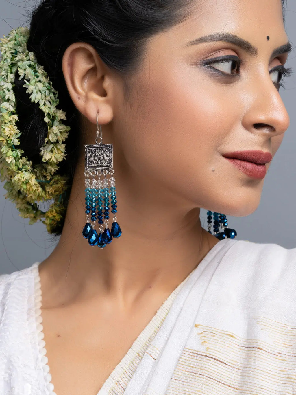 Handmade blue crystal earrings with intricate silver design worn by woman in traditional attire