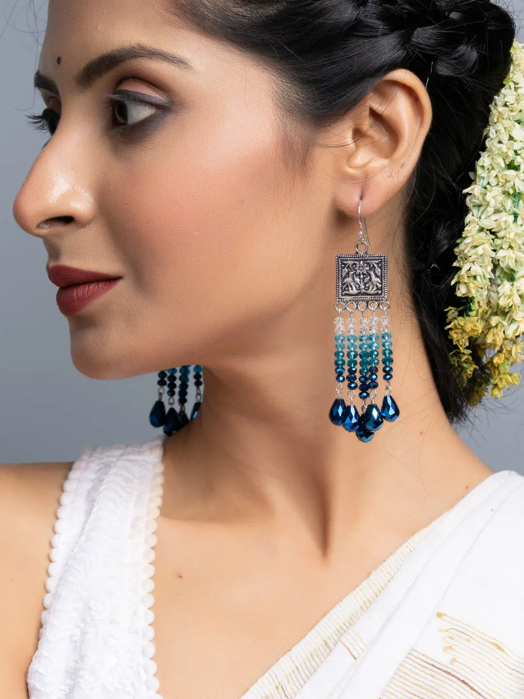Handmade blue crystal earrings hanging from a woman wearing traditional white attire and flowers in her hair