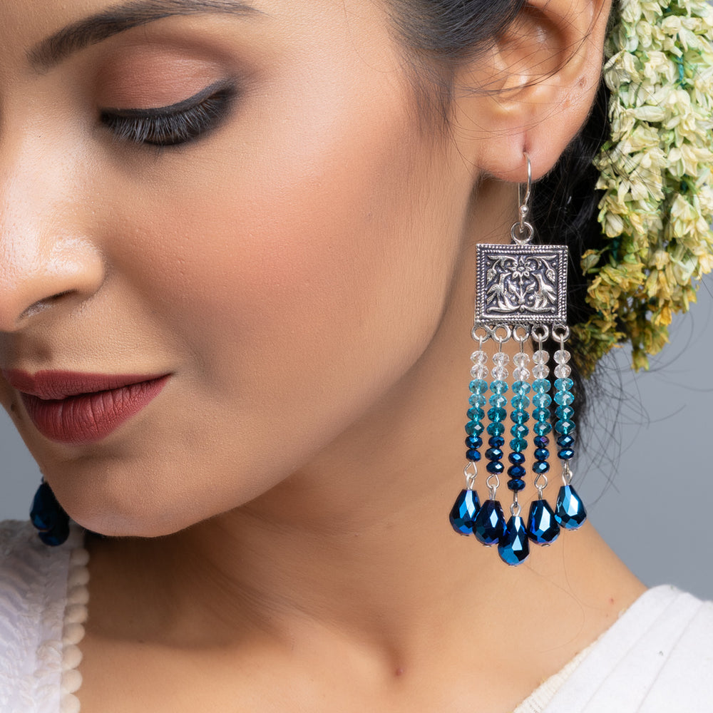 Close-up of handmade blue crystal earrings worn by a woman showcasing intricate beadwork and silver detailing