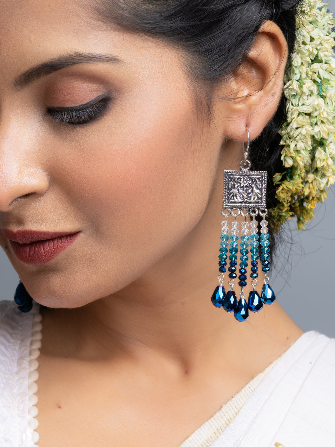Close-up of handmade blue crystal earrings worn by a woman showcasing intricate beadwork and silver detailing