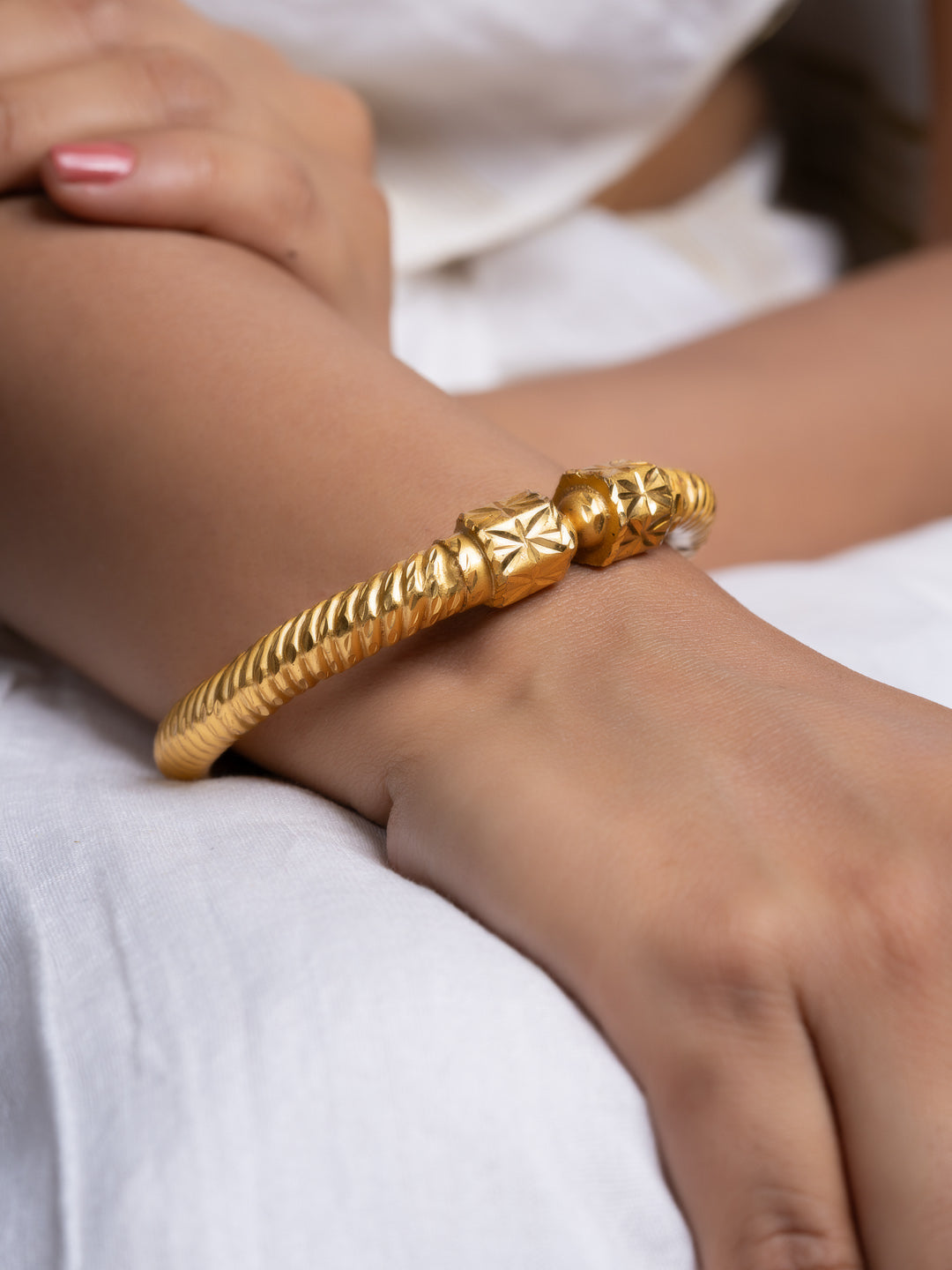 gold plate bangle from LOOK AND ADORN worn on a model wrist with twisted rope design and ornate end caps