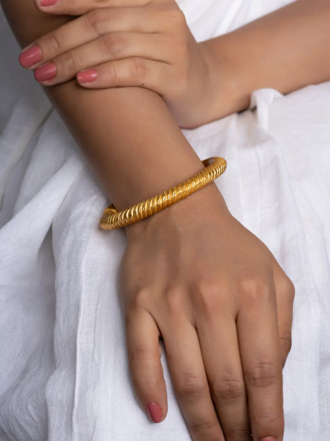 Model wearing a textured gold plate bangle on wrist over white linen dress showcasing shine and everyday elegance
