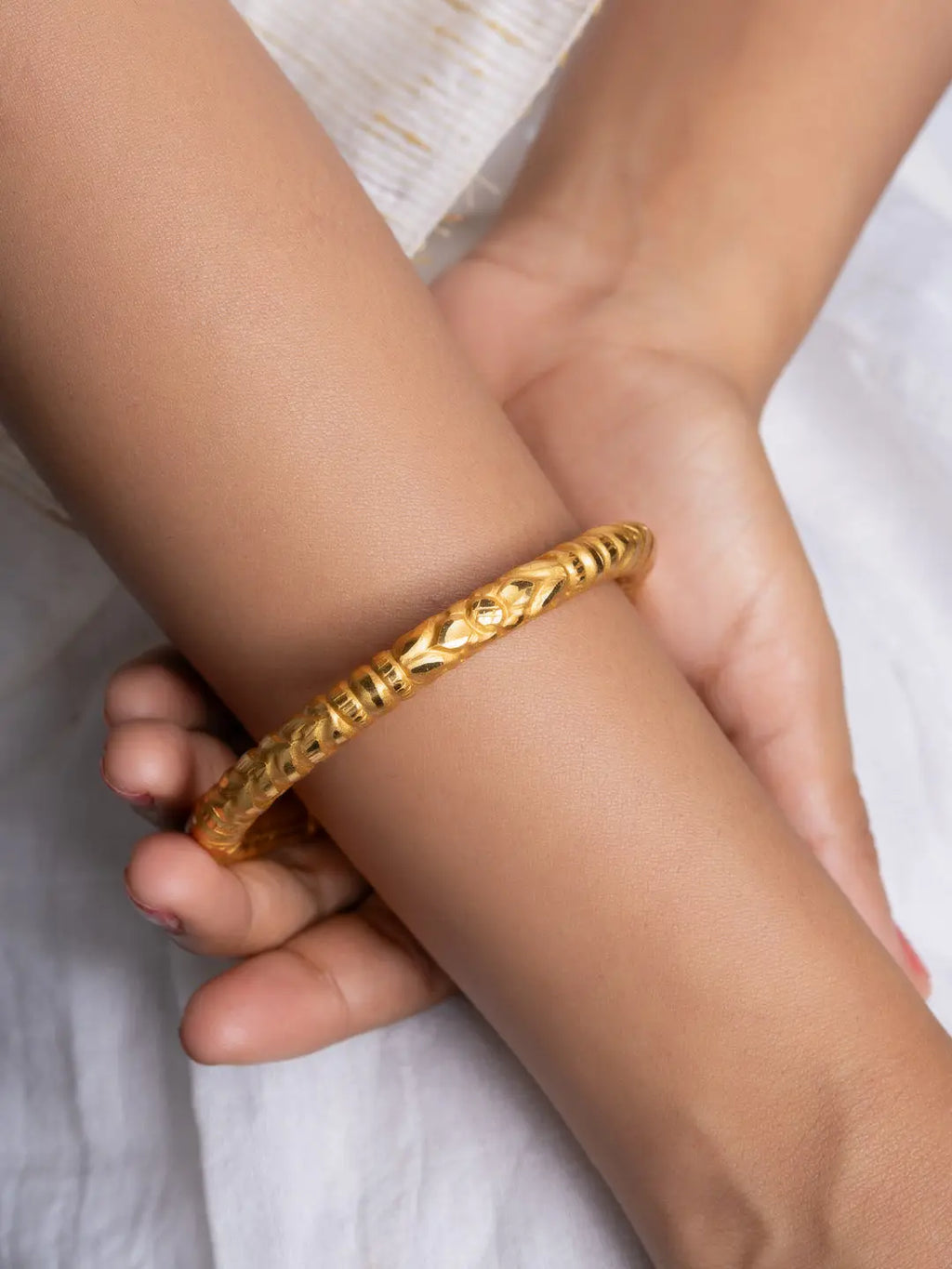 LOOK AND ADORN gold plated bangle on wrist with detailed carved floral pattern and polished finish