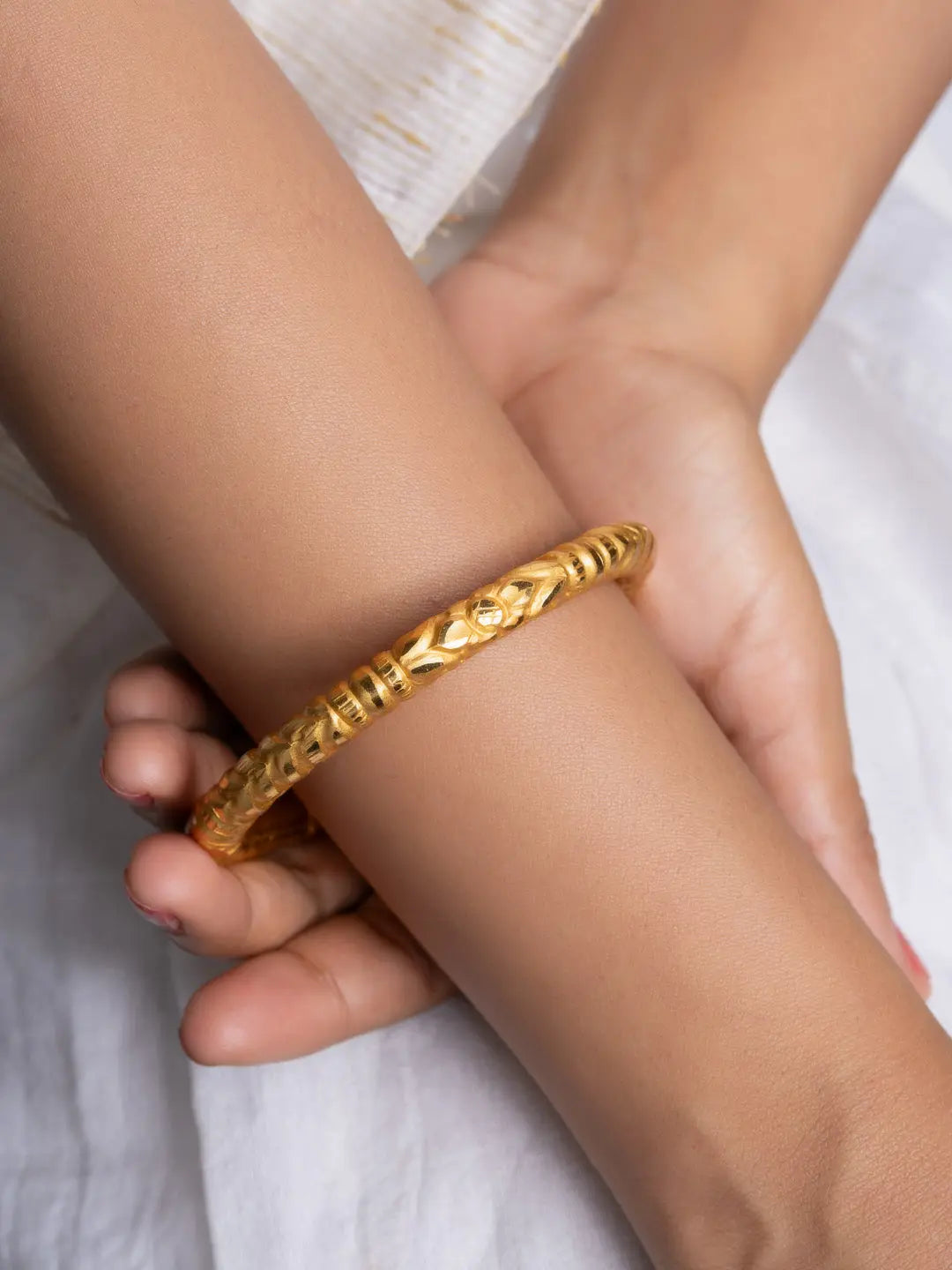 LOOK AND ADORN gold plated bangle on wrist with detailed carved floral pattern and polished finish