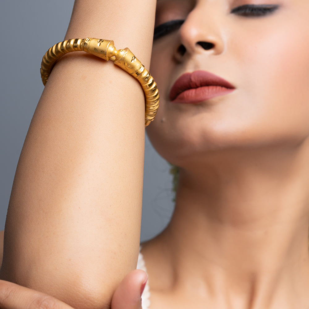 Close up of woman wearing gold plated bangle on forearm with textured ribbed design and polished finish