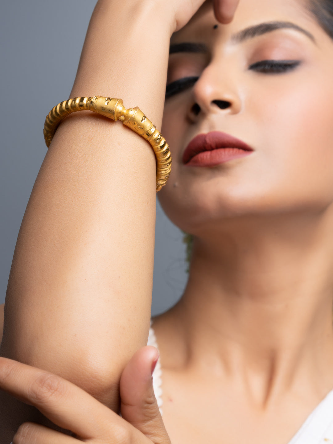 Close up of woman wearing gold plated bangle on forearm with textured ribbed design and polished finish
