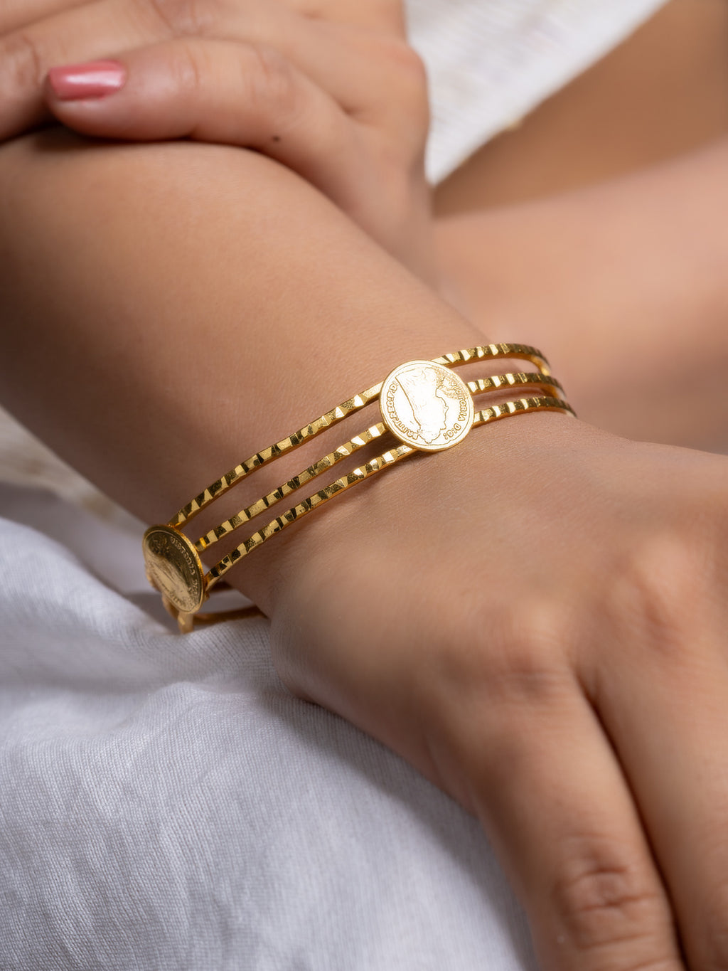 Model wrist wearing gold plated bangle with three textured bands and coin medallions for elegant everyday wear