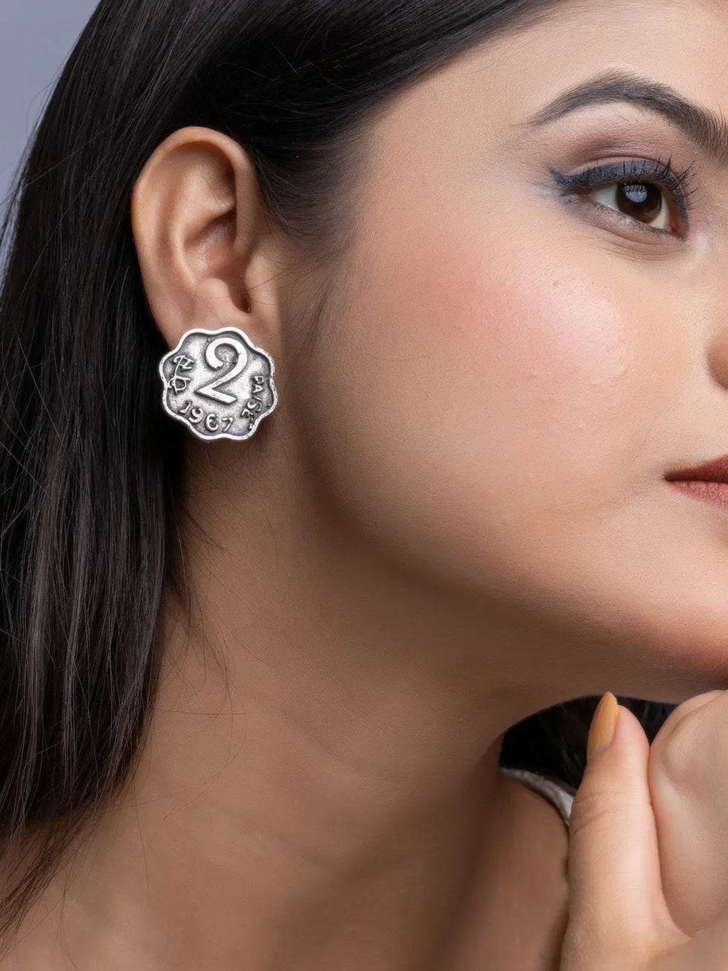 Close-up of oxidised silver earrings worn on a woman’s ear with floral and number two design