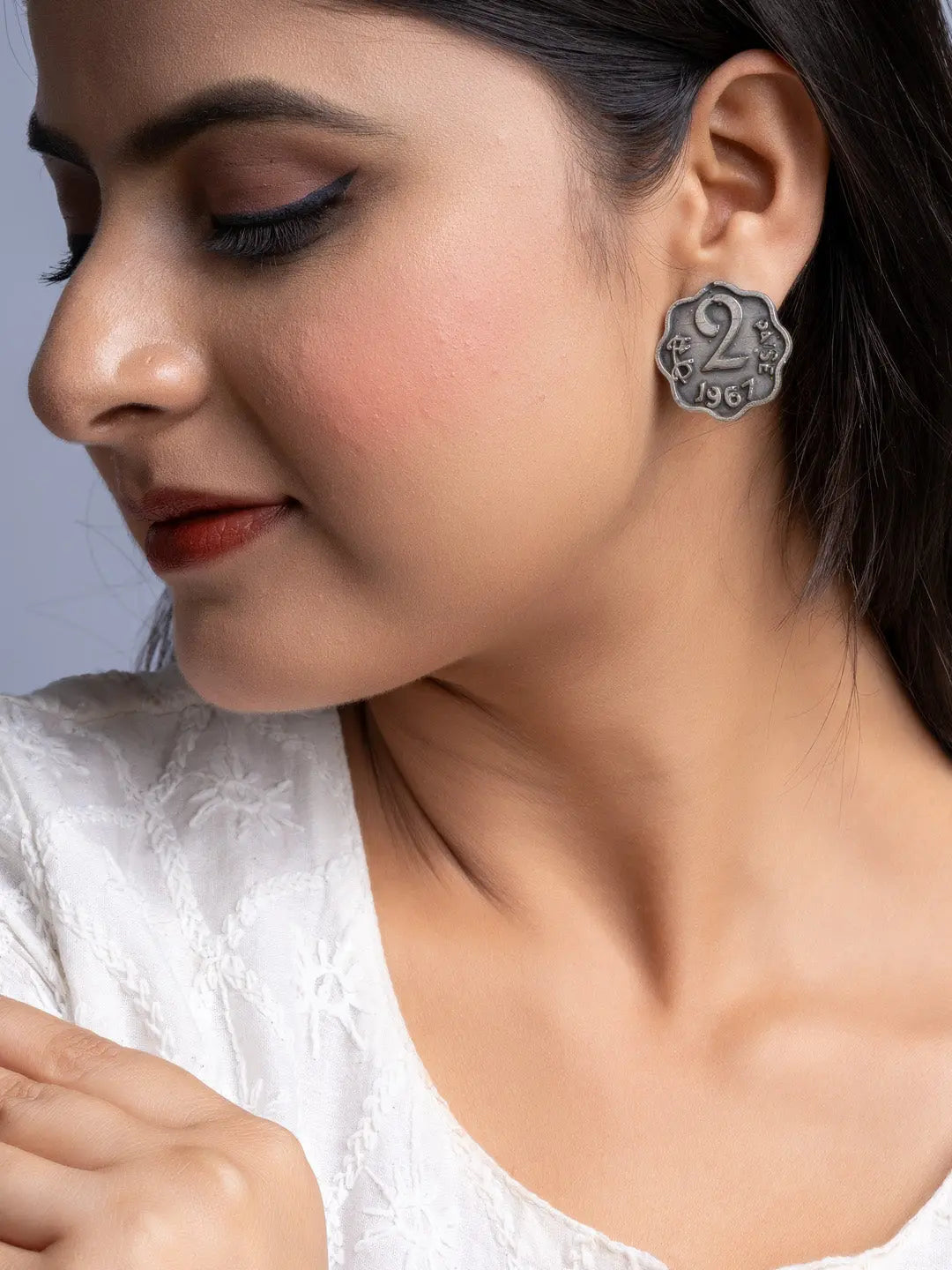 Close-up of woman wearing oxidised silver earrings shaped like vintage coins with intricate design