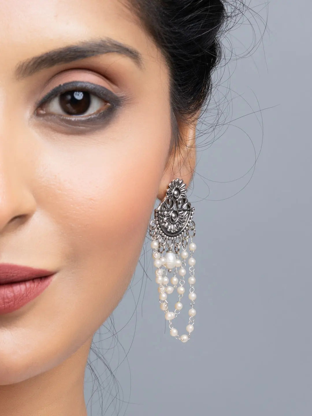 Handmade pearl stud earrings with intricate silver design and dangling pearls worn on woman's ear