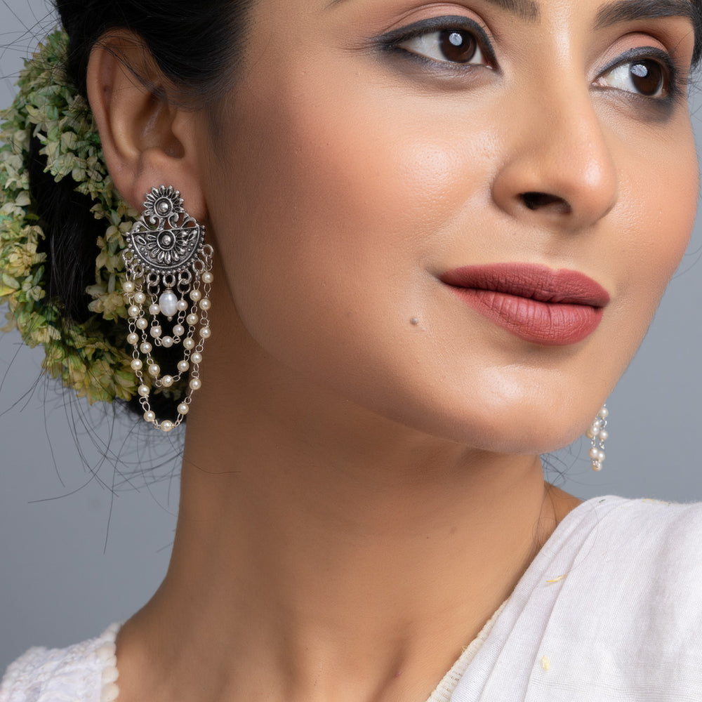 Close-up of woman wearing handmade pearl stud earrings with ornate silver detailing and white traditional attire