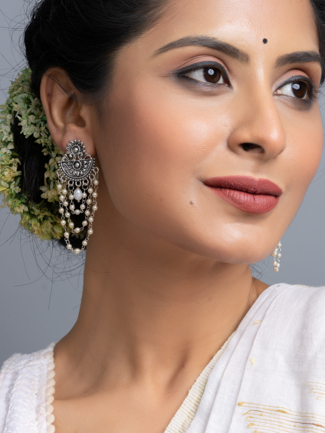Close-up of woman wearing handmade pearl stud earrings with ornate silver detailing and white traditional attire