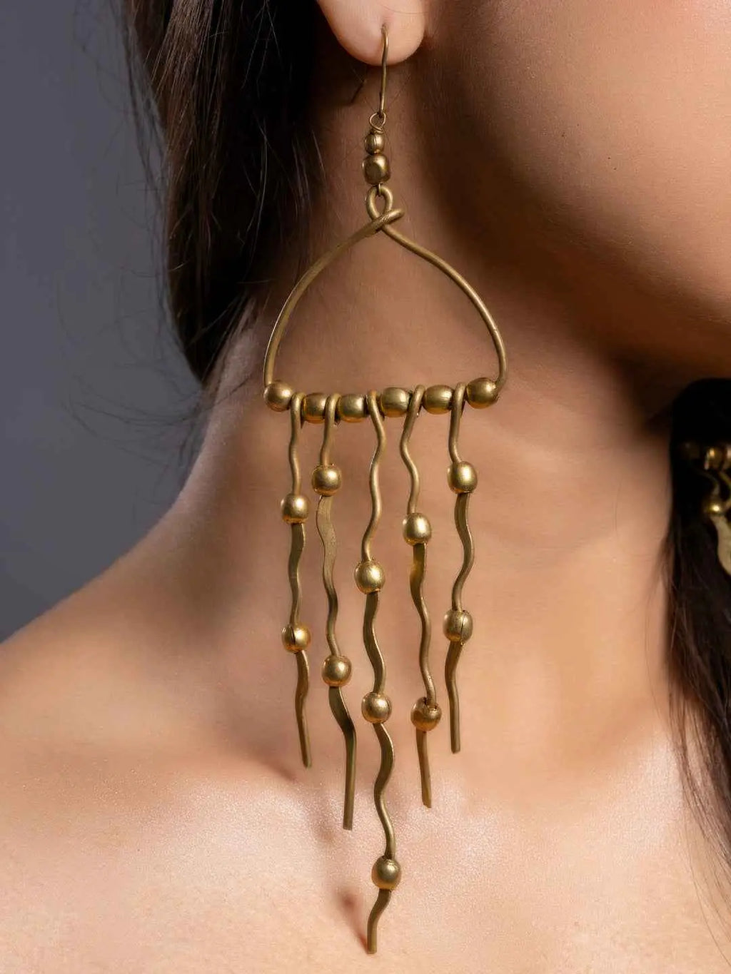 Dokra brass earrings with a unique wavy design and dangling ball accents in gold finish
