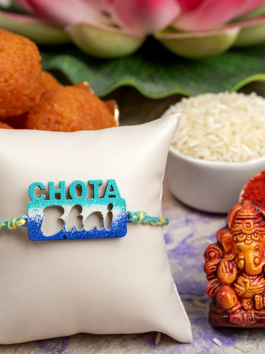 LOOK AND ADORN chhota bhai rakhi in blue with decorative background including sweets and Ganesh idol