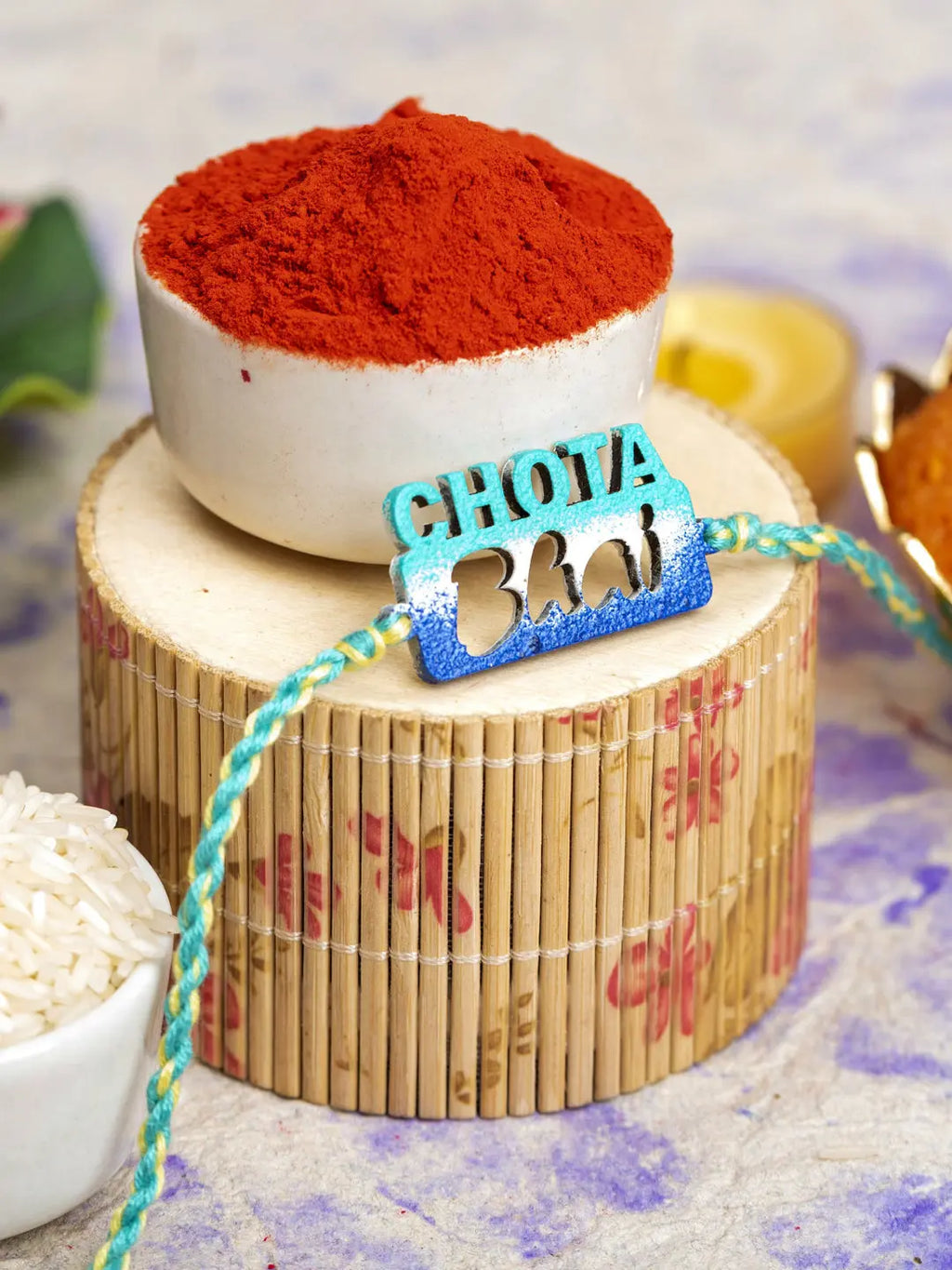 LOOK AND ADORN chhota bhai rakhi with blue and green thread placed on wooden decor with red powder in background
