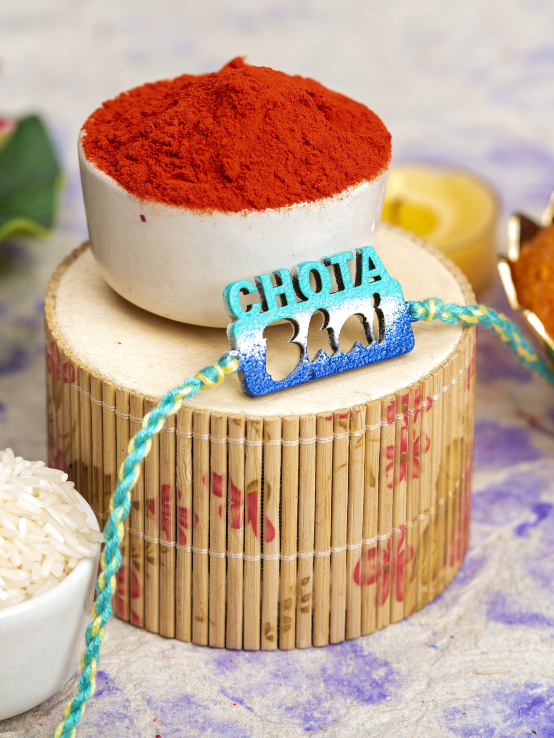 LOOK AND ADORN chhota bhai rakhi with blue and green thread placed on wooden decor with red powder in background