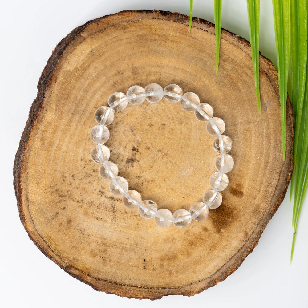 Clear quartz bracelet elegantly displayed on a wooden slice with green leaves for a natural look
