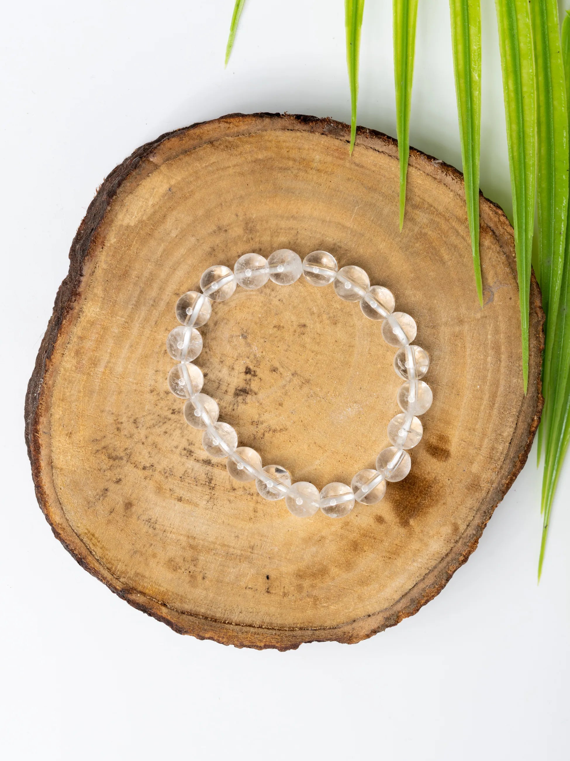 Clear quartz bracelet elegantly displayed on a wooden slice with green leaves for a natural look