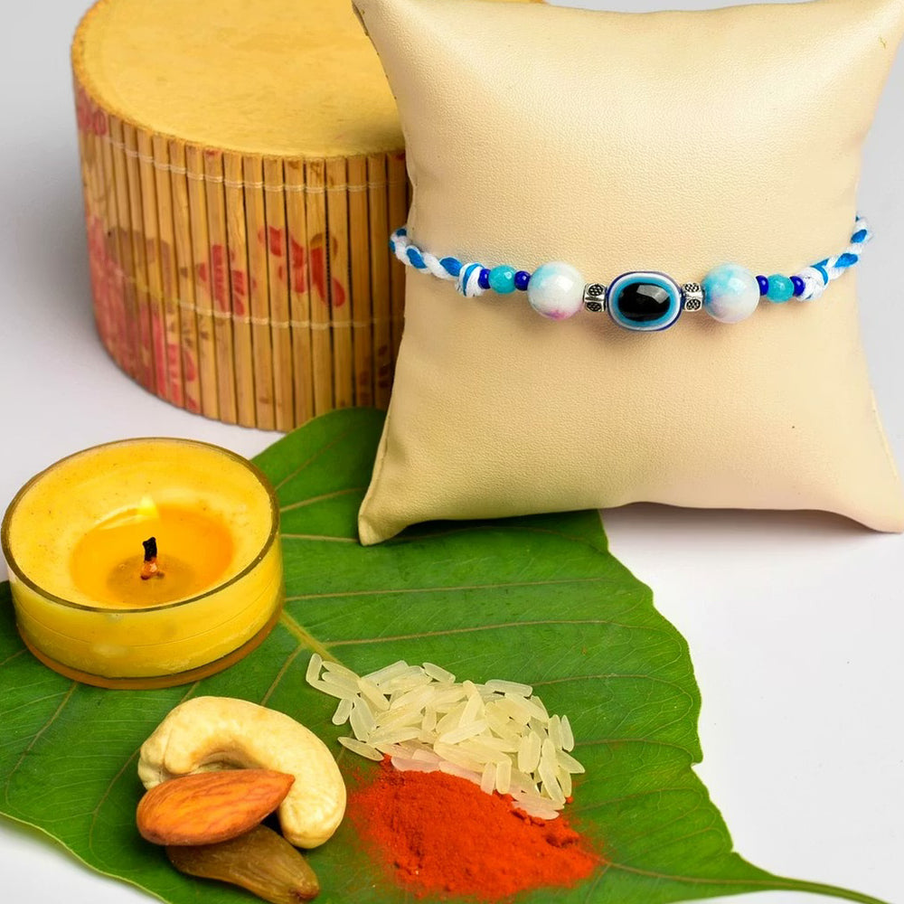 LOOK AND ADORN evil eye rakhi with blue beads displayed on a cushion with traditional pooja items on a green leaf