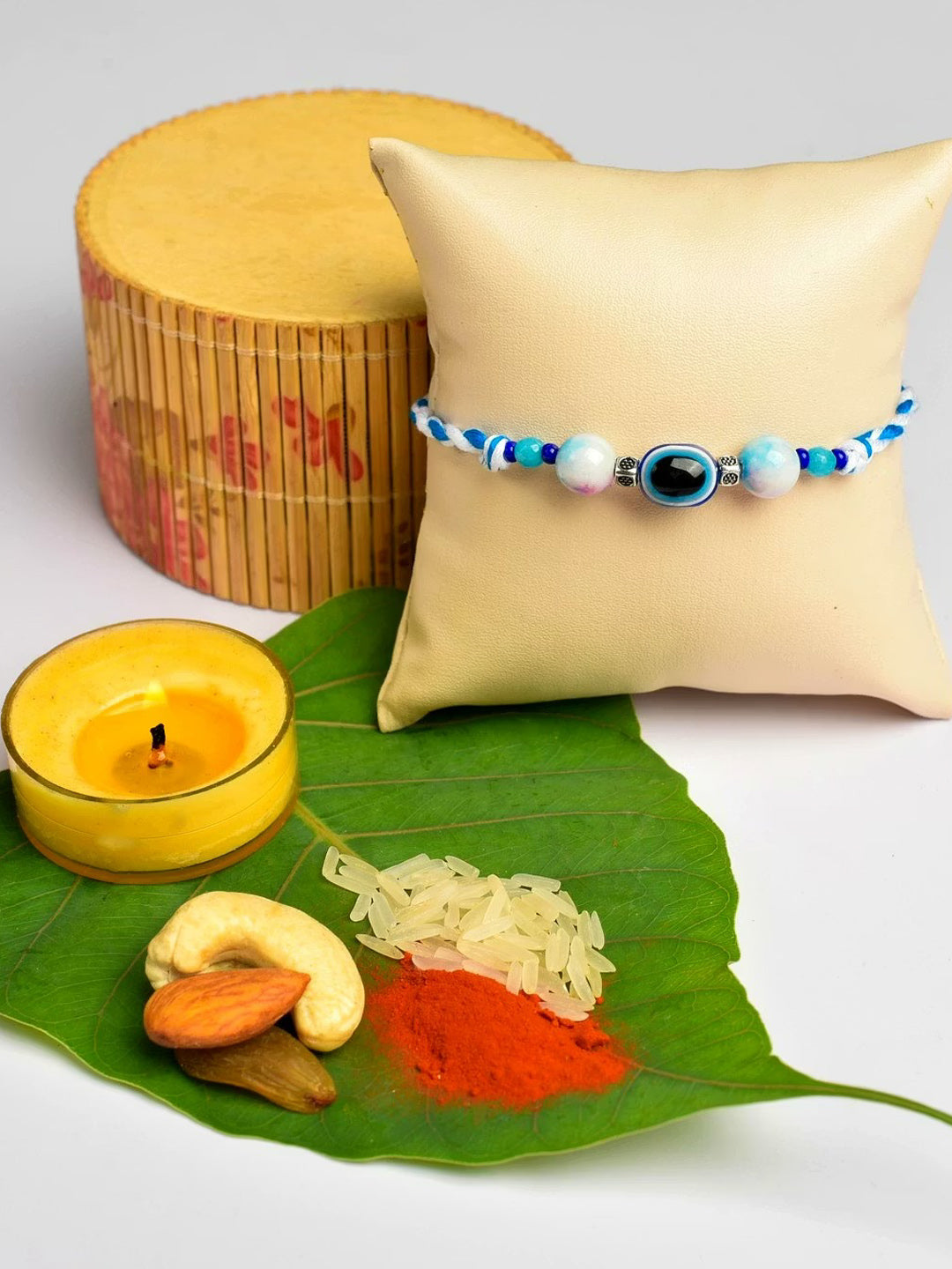 LOOK AND ADORN evil eye rakhi with blue beads displayed on a cushion with traditional pooja items on a green leaf