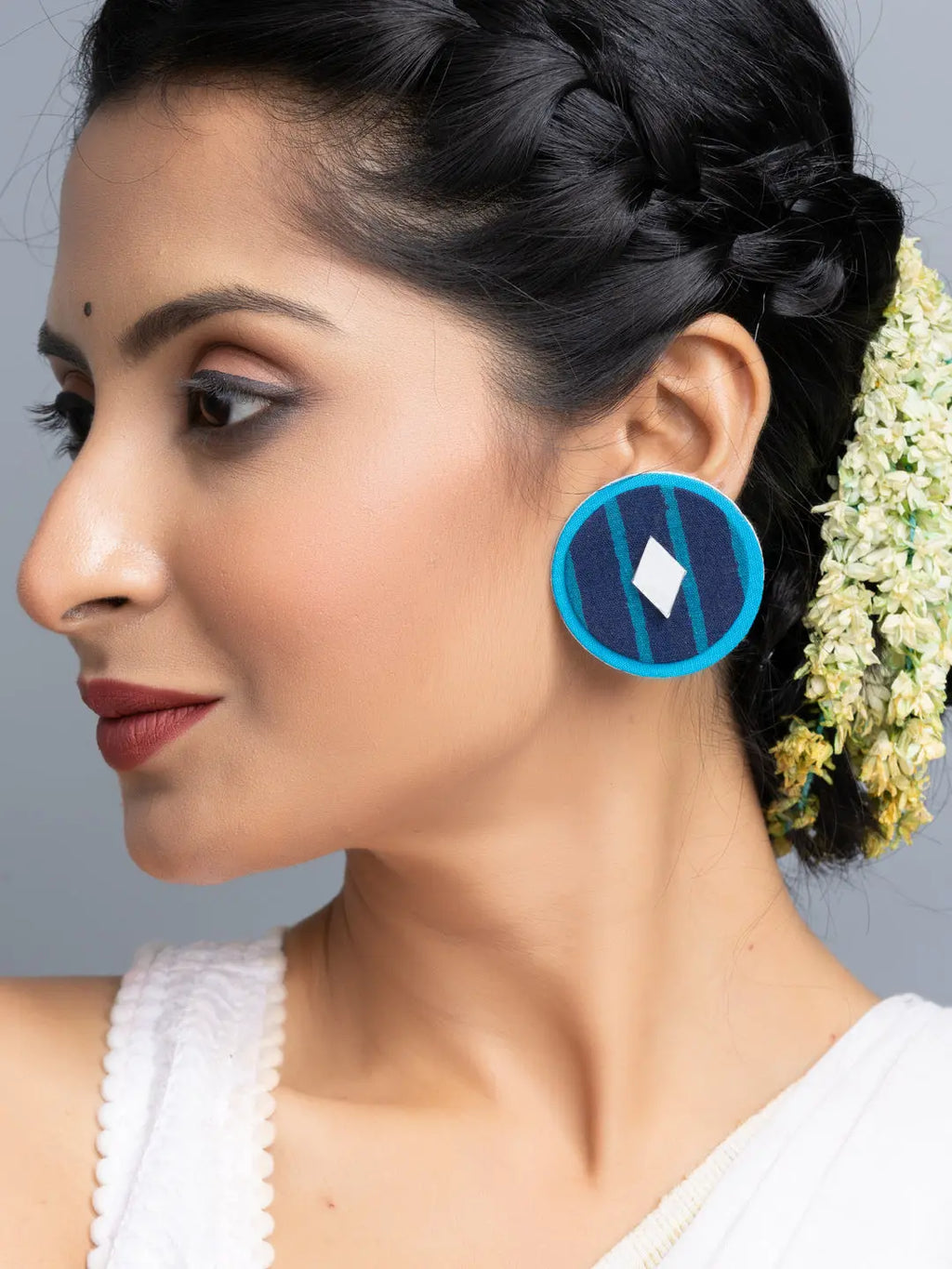 Handmade fabric earrings in blue and turquoise worn by woman with braided hair and white outfit
