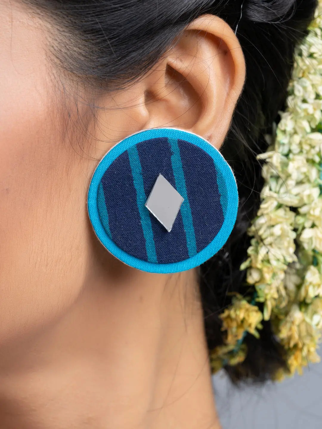 Handmade fabric earrings in blue with a geometric design worn by a person with floral hair accessories