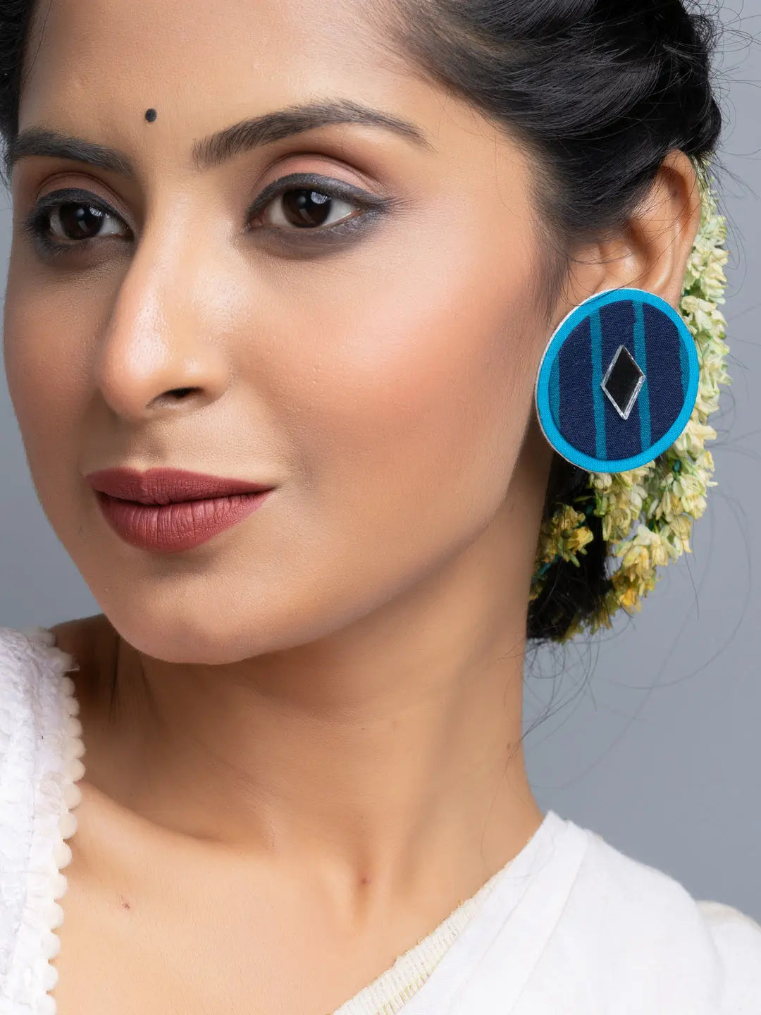Woman wearing handmade blue fabric earrings with geometric design and flowers in hair