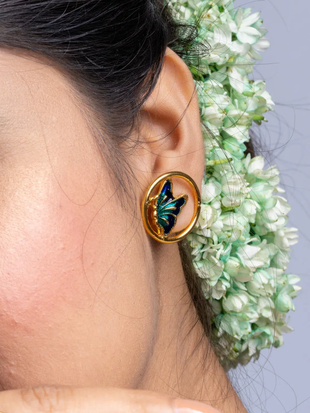 LOOK AND ADORN gold plated earrings featuring butterfly design worn on ear with white floral background