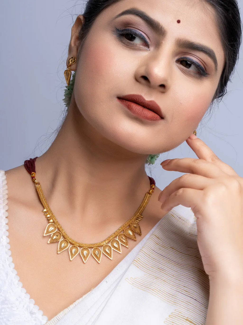 Woman wearing a gold plated necklace set from LOOK AND ADORN with intricate leaf-shaped designs