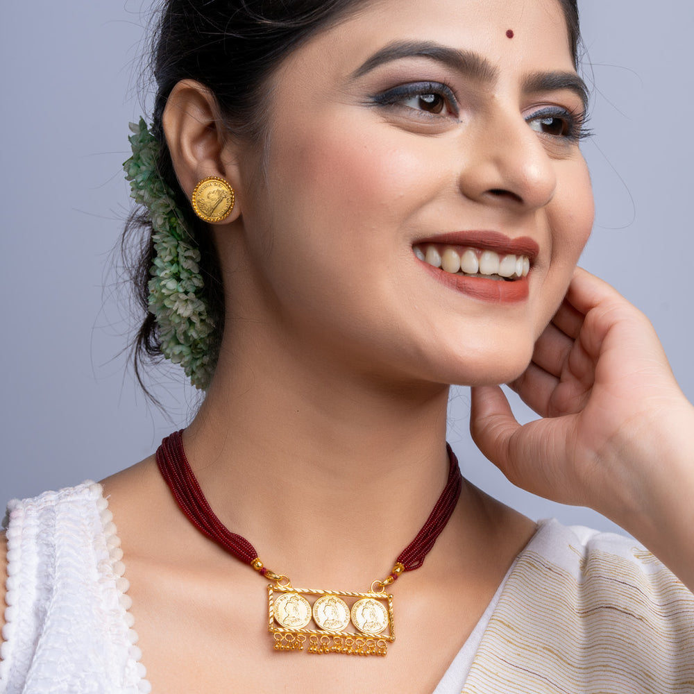Woman wearing a gold plated necklace set with red cords and matching gold earrings from LOOK AND ADORN