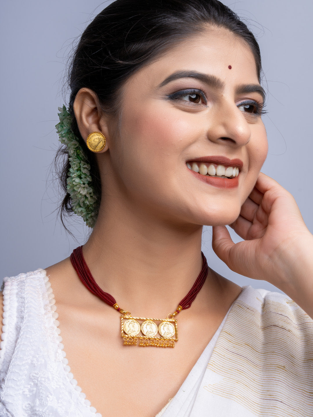 Woman wearing a gold plated necklace set with red cords and matching gold earrings from LOOK AND ADORN