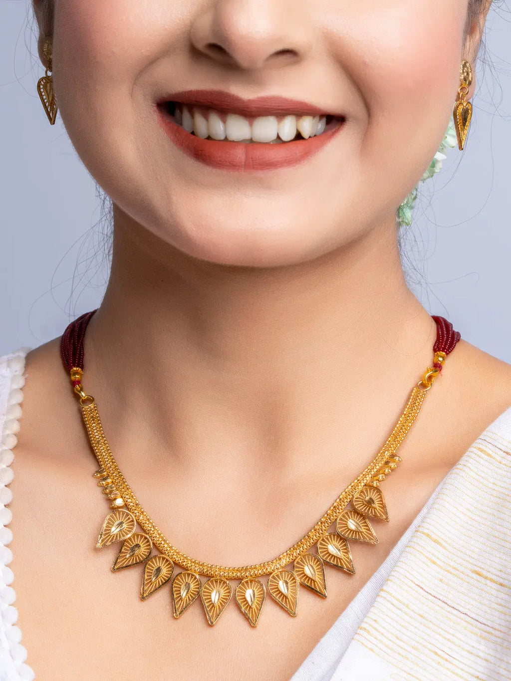 Elegant gold plated necklace set with intricate leaf design worn by smiling woman