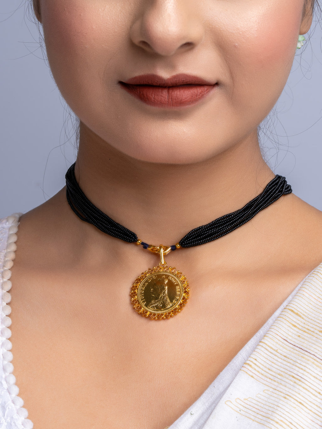 Gold plated pendant with intricate design on black beaded necklace worn by woman