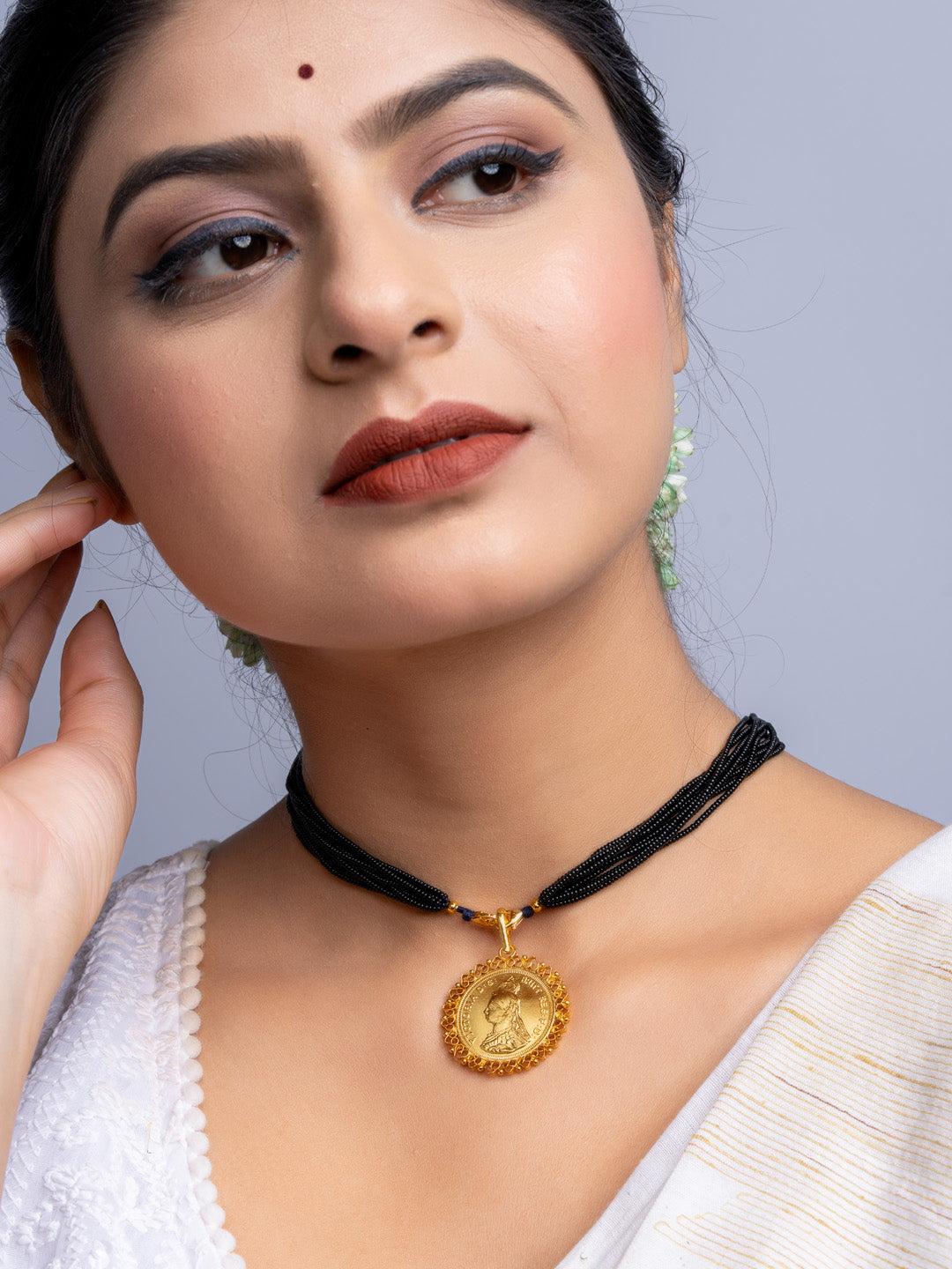 Woman wearing a gold plated pendant on a black multi-strand necklace with traditional attire